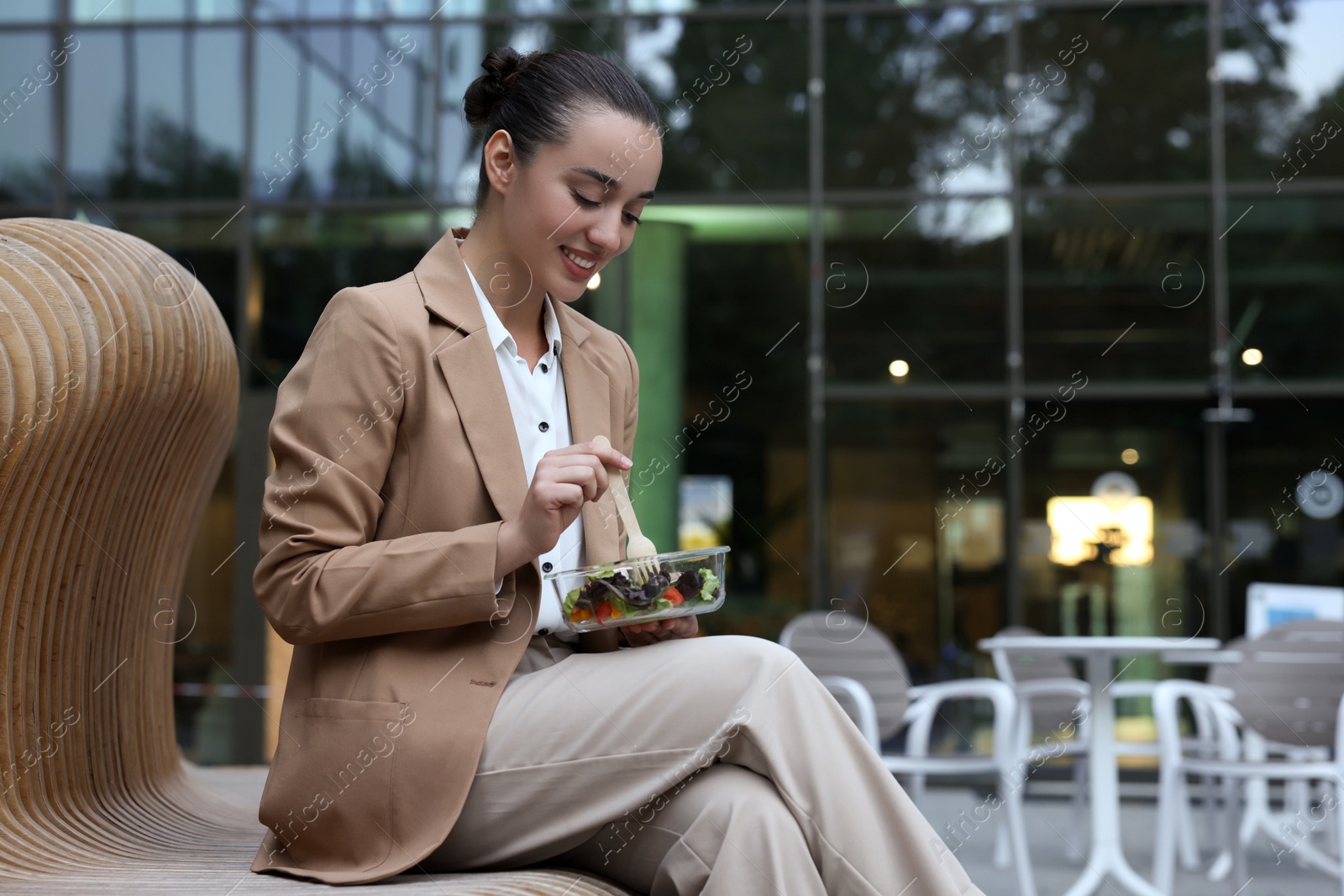 Photo of Happy young businesswoman eating lunch on bench outdoors