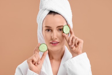 Photo of Beautiful woman in bathrobe with pieces of cucumber on beige background