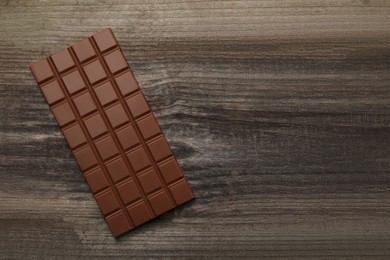 Photo of Delicious milk chocolate bar on wooden table, top view. Space for text