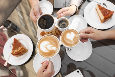 Friends drinking coffee at wooden table in outdoor cafe, top view