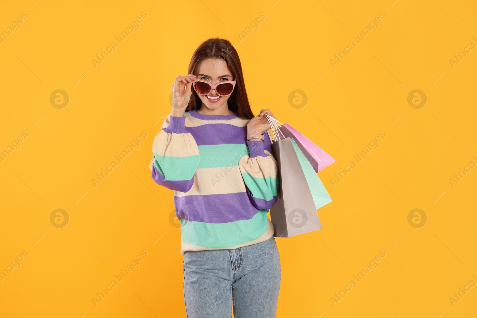 Photo of Happy young woman with shopping bags on yellow background. Big sale