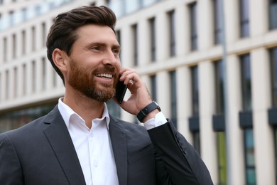 Photo of Handsome businessman talking on smartphone while walking outdoors, space for text