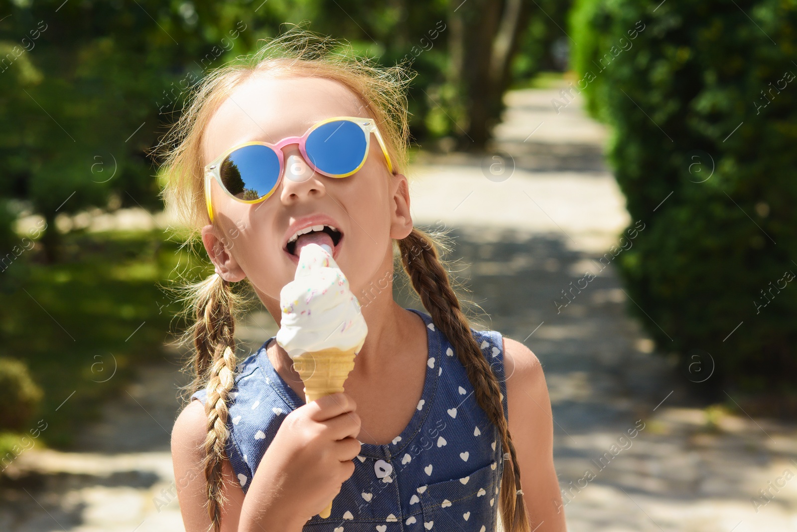 Photo of Adorable little girl eating delicious ice cream outdoors on sunny summer day, space for text