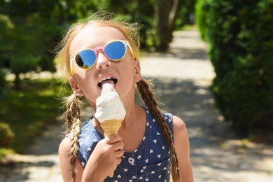 Photo of Adorable little girl eating delicious ice cream outdoors on sunny summer day, space for text