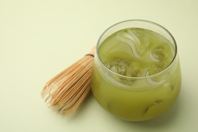 Photo of Glass of delicious iced matcha tea and bamboo whisk on green background, closeup. Space for text