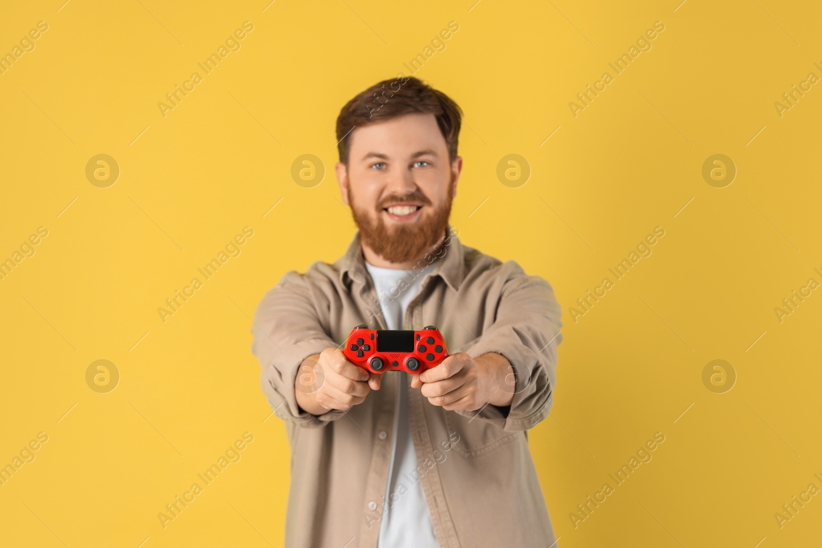 Photo of Smiling man with game controller on pale yellow background, selective focus