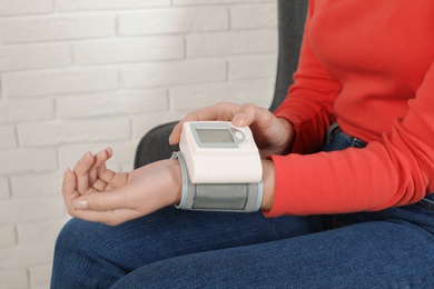 Photo of Young woman checking pulse with digital medical device against brick wall, closeup. Space for text