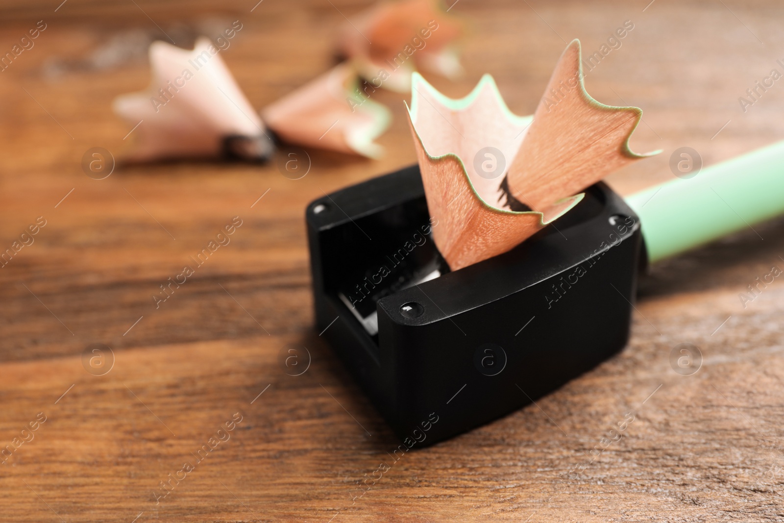 Photo of Black sharpener with pencil shavings on wooden table, closeup. Space for text