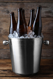 Photo of Metal bucket with beer and ice cubes on wooden table