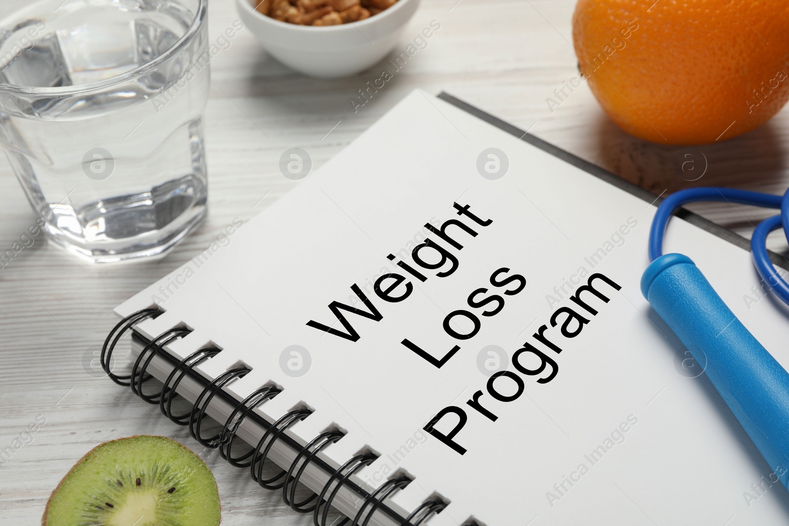 Photo of Weight loss concept. Composition with notebook, skipping rope, glass of water and fruits on white wooden table, closeup