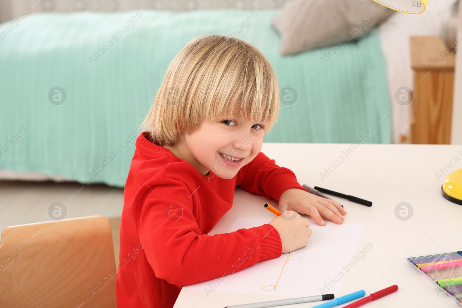 Photo of Little boy drawing at desk in room. Home workplace