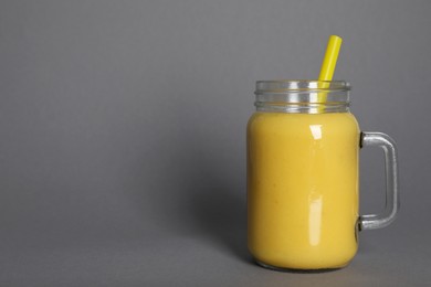 Photo of Mason jar of tasty smoothie with straw on grey background. Space for text