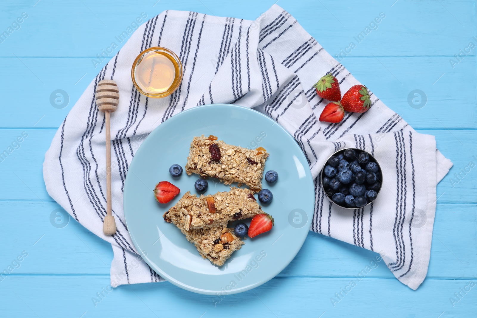 Photo of Tasty granola bars with berries and honey on light blue wooden table, flat lay