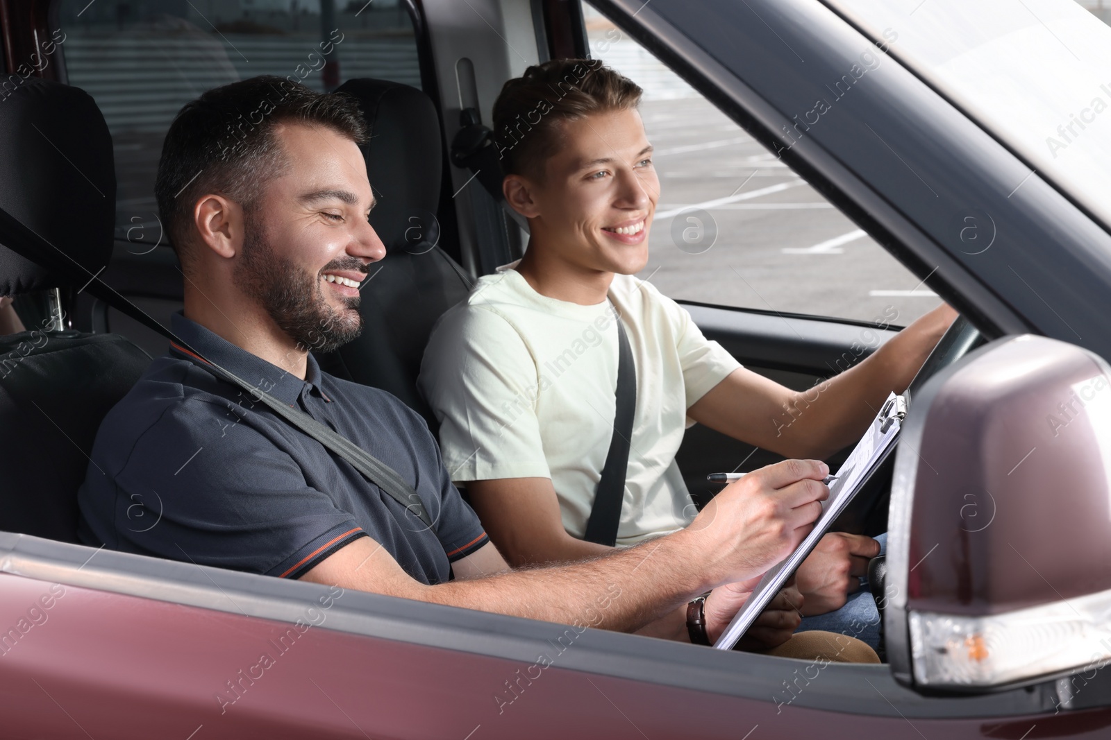 Photo of Driving school. Happy student passing driving test with examiner in car at parking lot