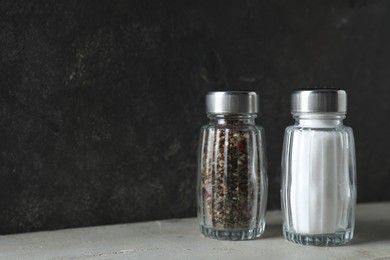 Photo of Salt and pepper shakers on light table against grey background, closeup. Space for text