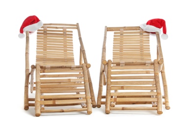 Photo of Wooden deck chairs and Santa Claus hats on white background. Christmas vacation