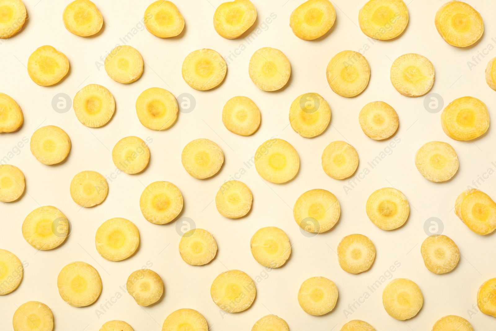 Photo of Slices of raw yellow carrot on beige background, flat lay