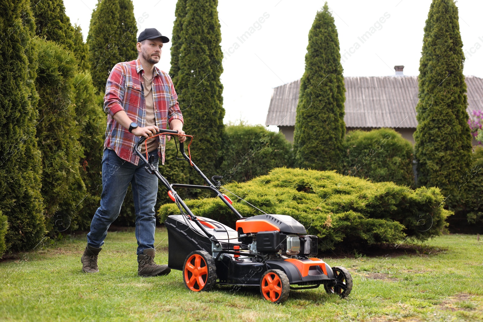 Photo of Man cutting green grass with lawn mower in garden