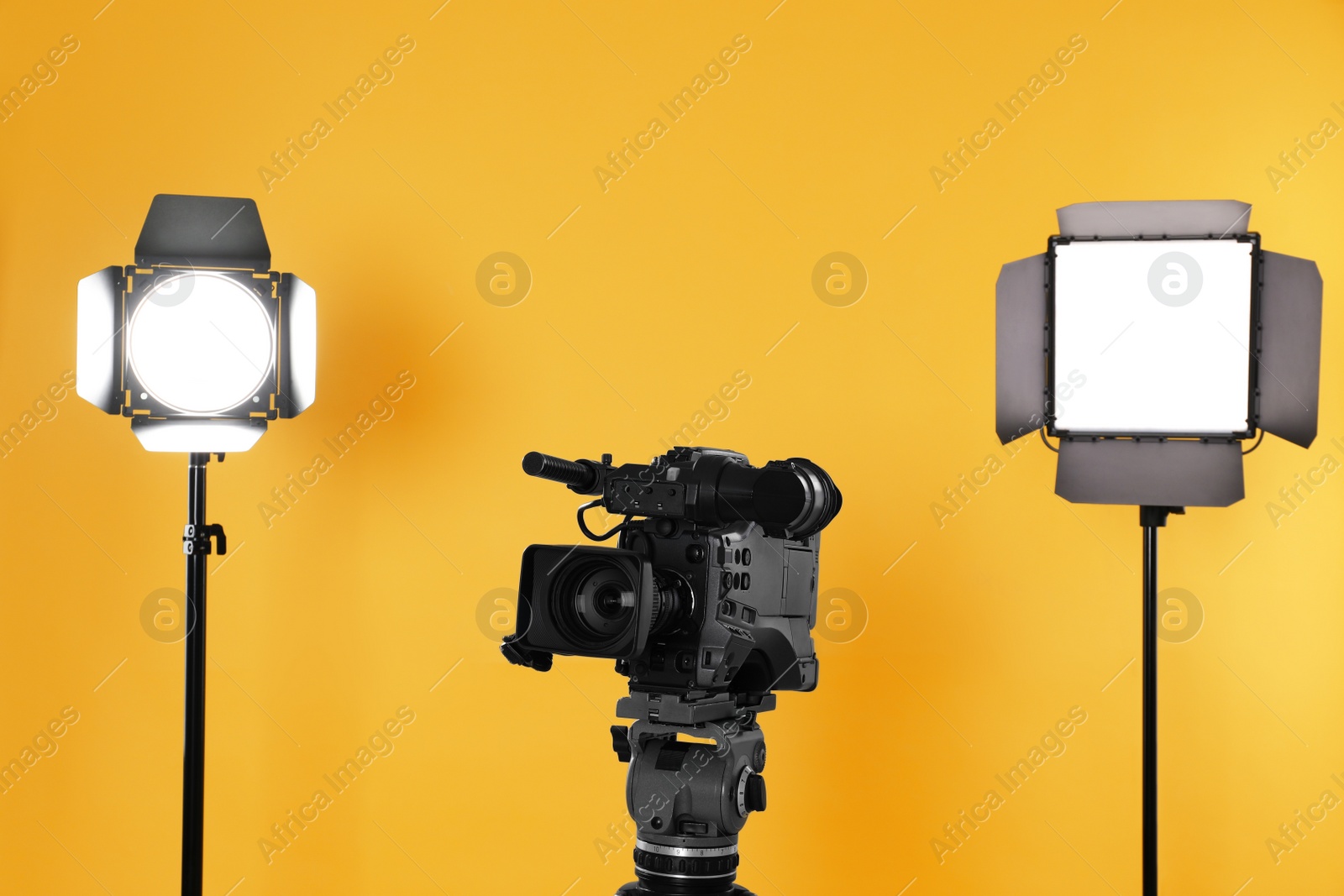 Photo of Professional video camera and lighting equipment on yellow background