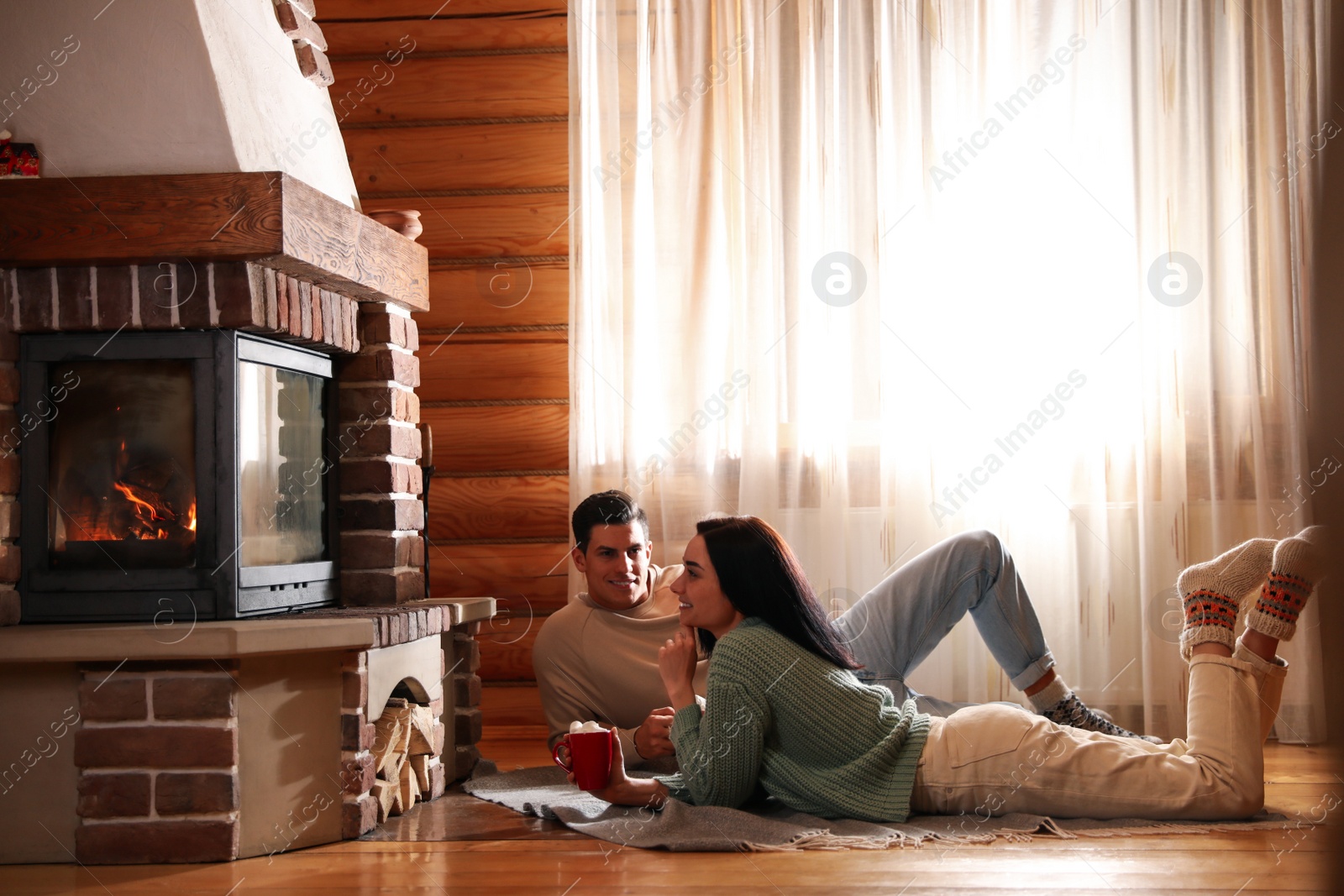 Photo of Lovely couple with delicious cocoa near fireplace on floor at home. Winter vacation