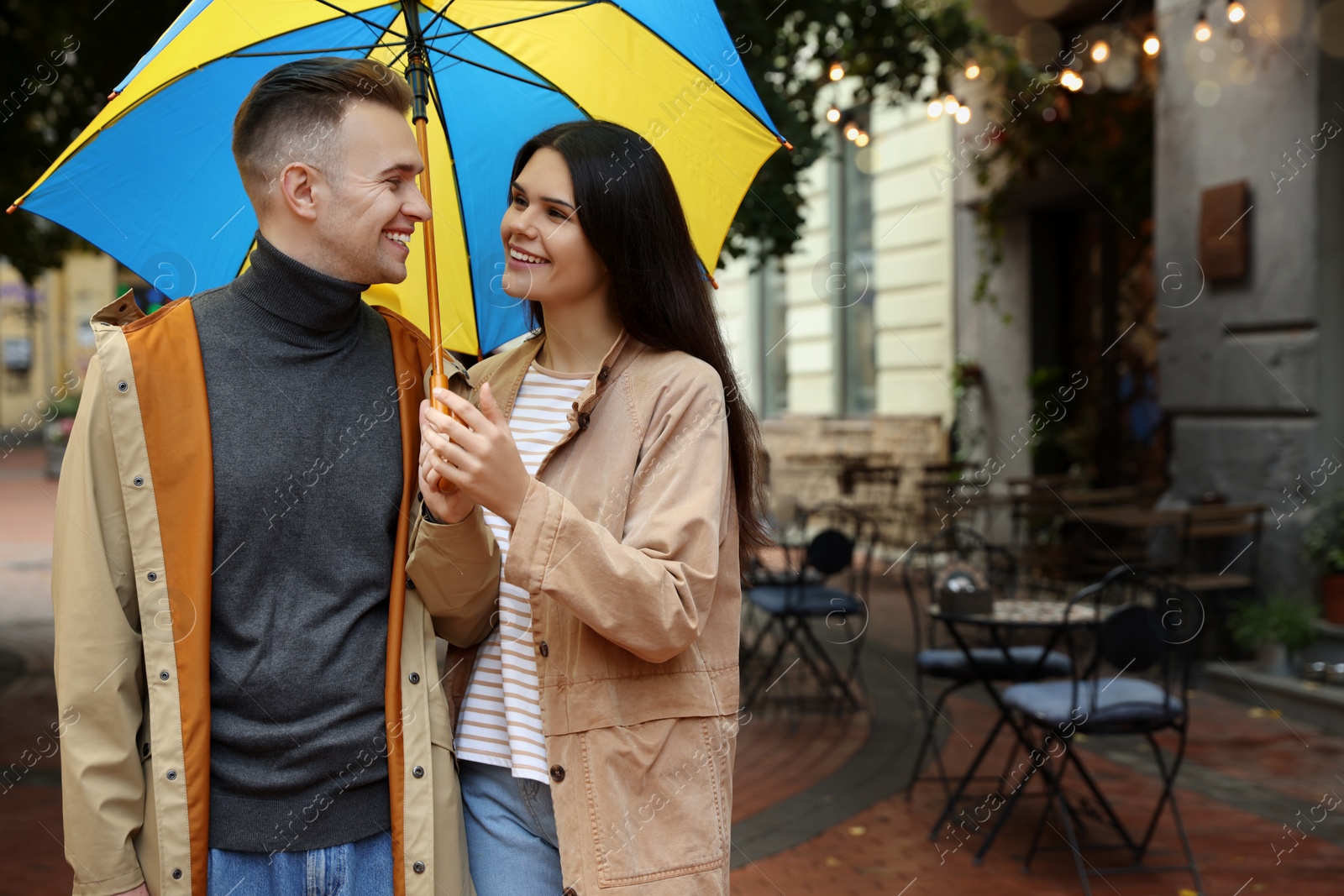 Photo of Lovely young couple with umbrella walking under rain on city street