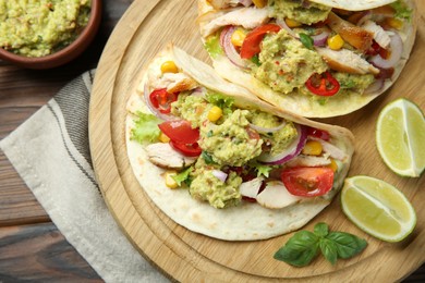 Photo of Delicious tacos with guacamole, meat and vegetables served with lime on wooden table, top view