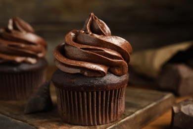 Photo of Delicious chocolate cupcakes with cream on wooden board, closeup