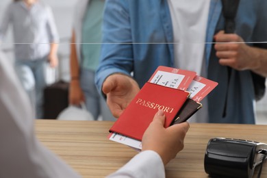 Agent giving passports with tickets to client at check-in desk in airport, closeup
