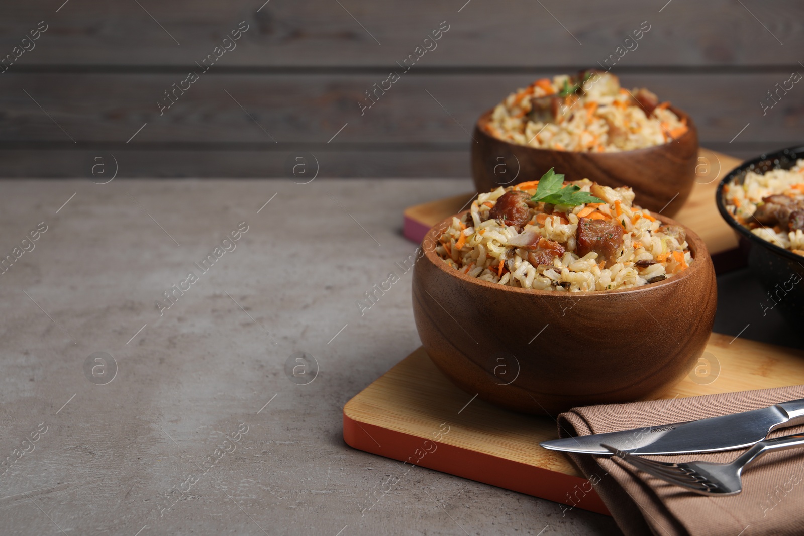 Photo of Delicious pilaf with meat and carrot in bowl on grey textured table. Space for text