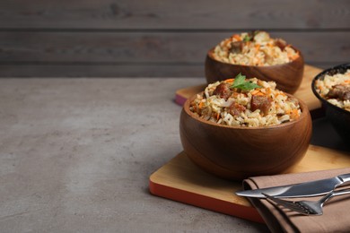 Delicious pilaf with meat and carrot in bowl on grey textured table. Space for text