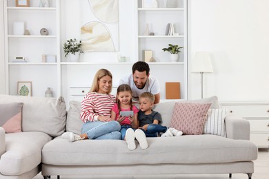 Photo of Happy family with smartphone spending time together on sofa at home