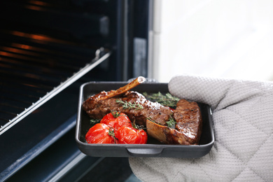 Photo of Chef taking delicious roasted ribs out of oven, closeup