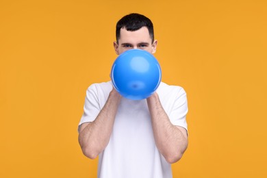 Photo of Young man inflating light blue balloon on yellow background