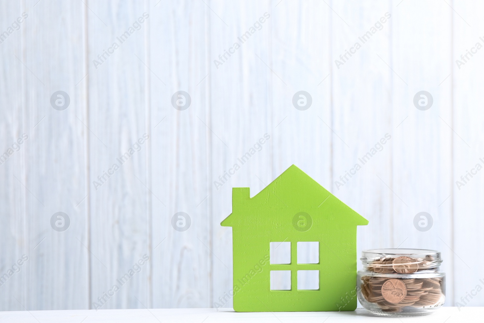 Photo of House model and jar with coins on table against wooden background. Space for text