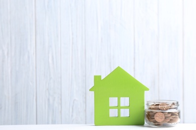 Photo of House model and jar with coins on table against wooden background. Space for text