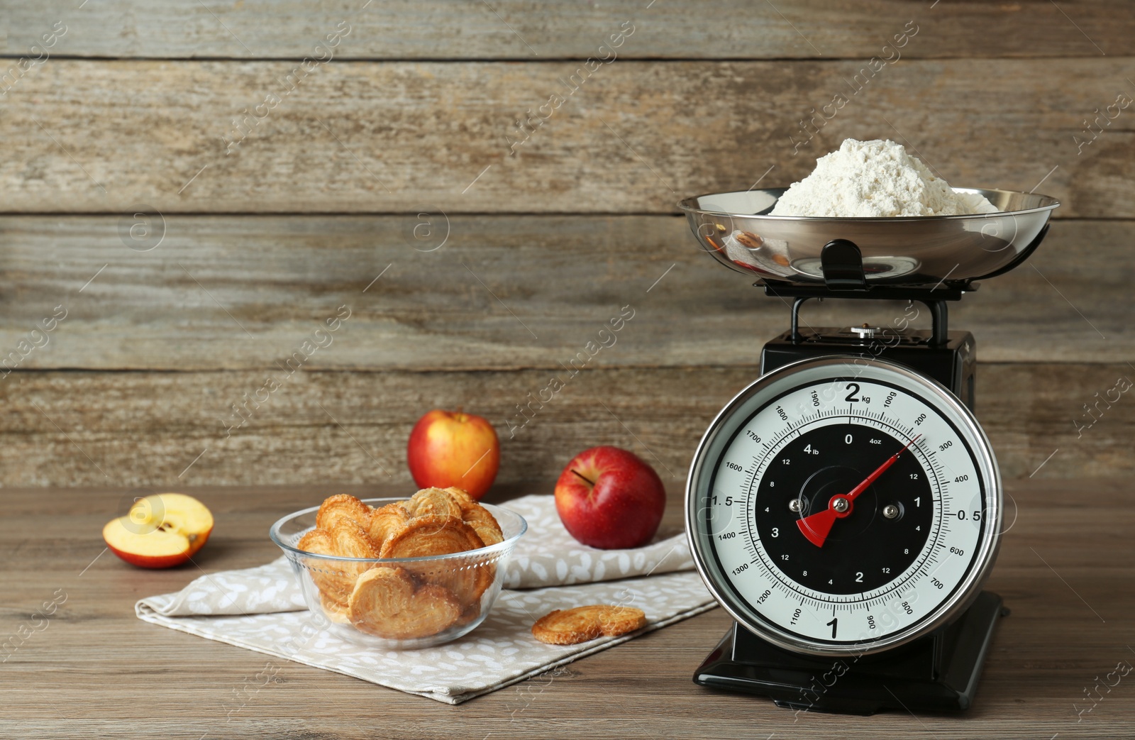 Photo of Kitchen scale with flour, cookies and apples on wooden table