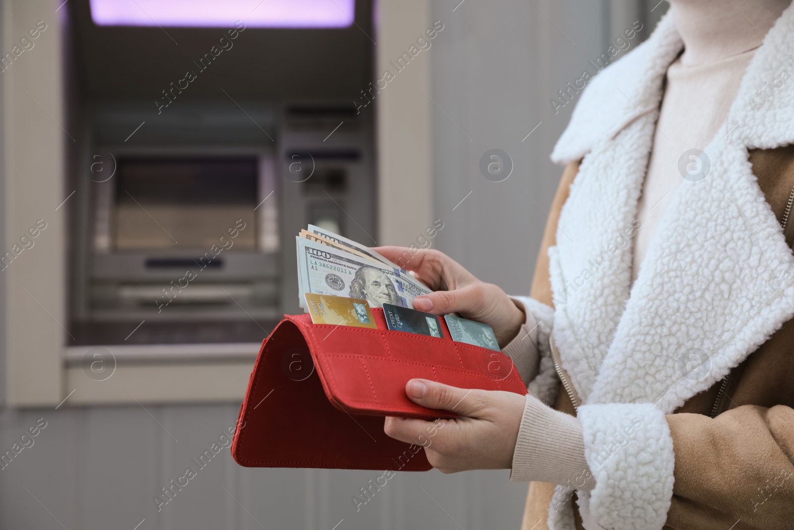 Photo of Woman putting money into wallet near cash machine outdoors, closeup