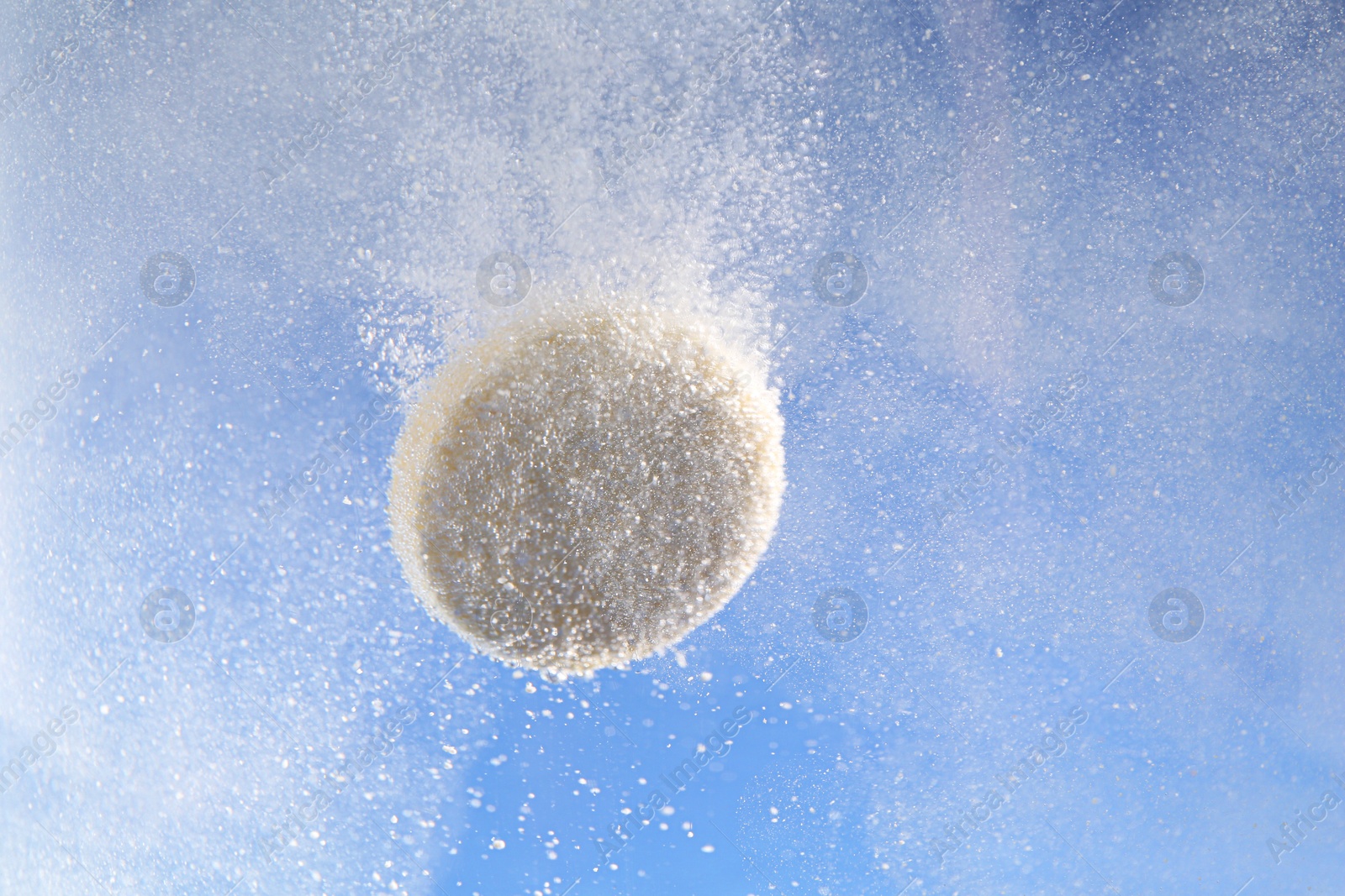 Photo of Effervescent pill dissolving in water on light blue background, closeup