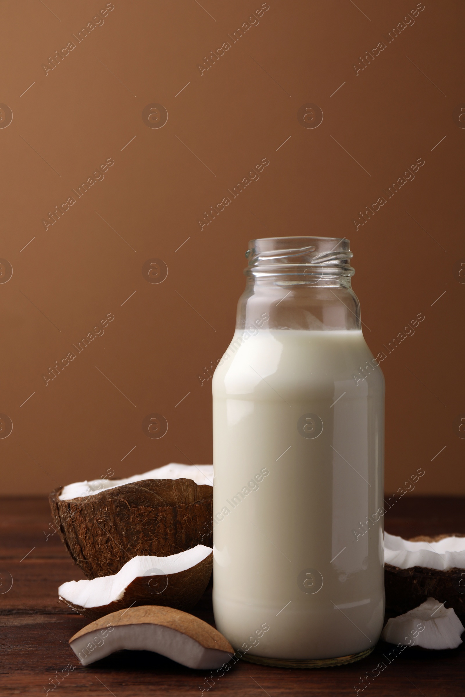 Photo of Bottle of delicious vegan milk and coconut pieces on wooden table