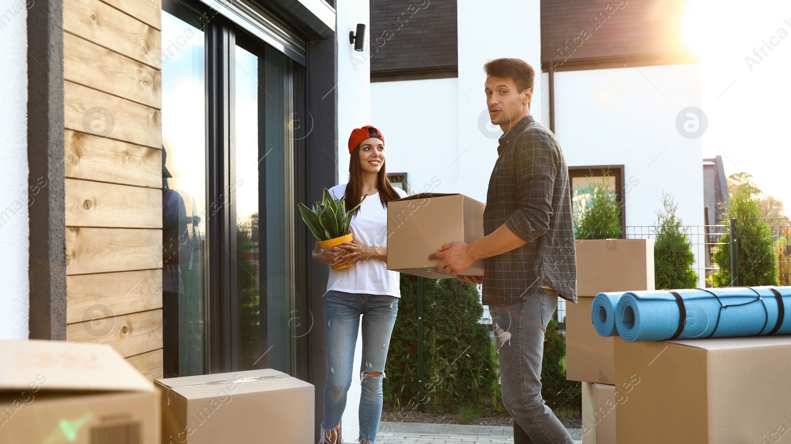 Photo of Happy couple with moving boxes and household stuff near their new house on sunny day