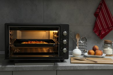 Open electric oven with delicious pie on countertop in kitchen