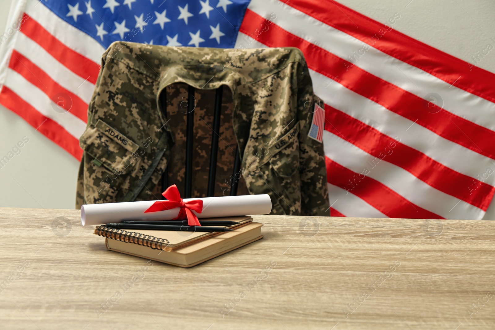 Photo of Diploma, notebooks and soldier uniform near flag of United States. Military education