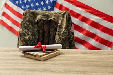 Photo of Diploma, notebooks and soldier uniform near flag of United States. Military education