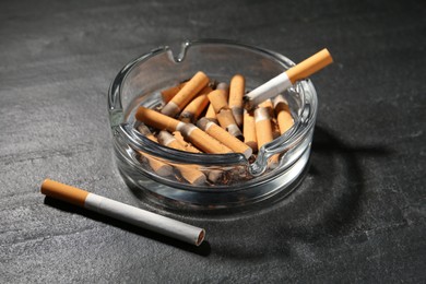 Photo of Glass ashtray with cigarette stubs on dark grey table