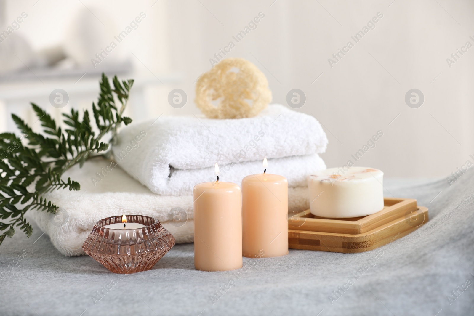 Photo of Spa composition. Burning candles, soap, towels and loofah on soft grey surface