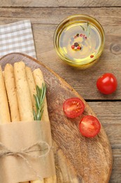 Photo of Tasty grissini with rosemary, oil and tomatoes on wooden table, flat lay