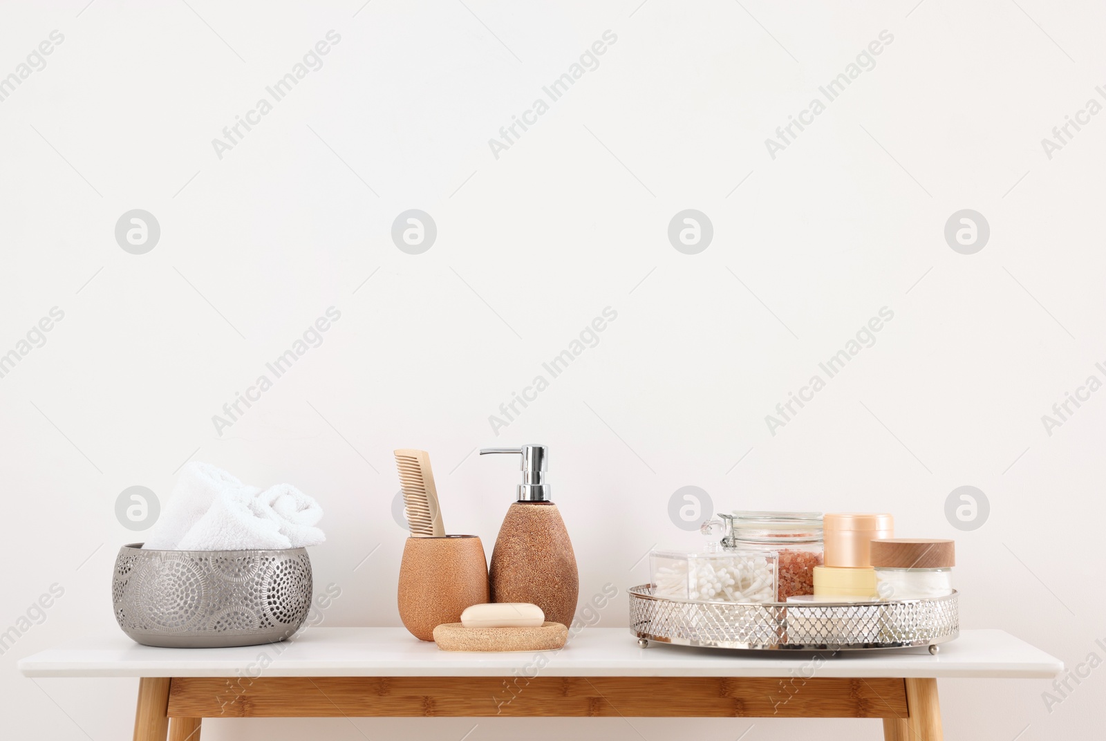 Photo of Different bath accessories and personal care products on table near white wall