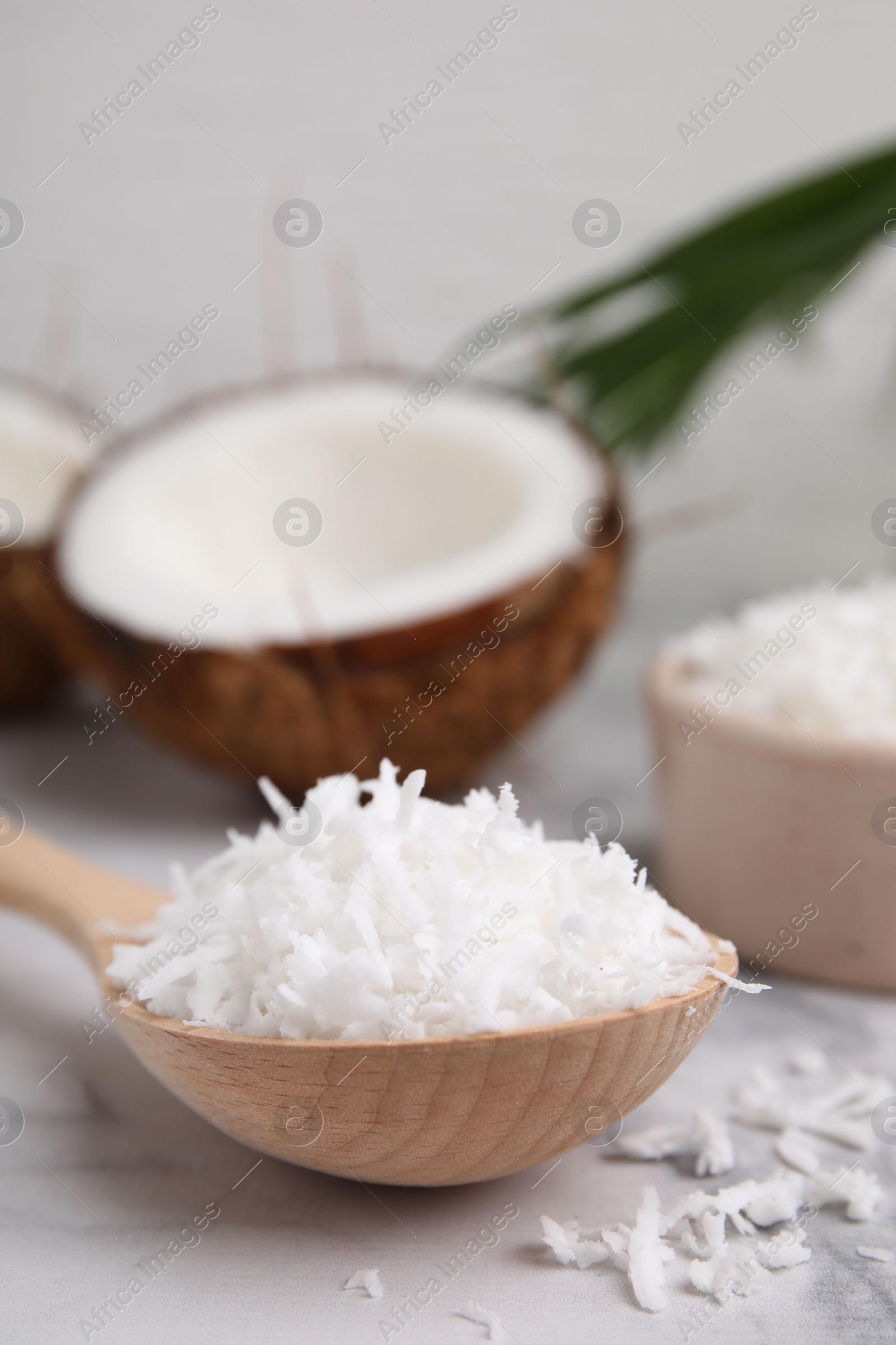 Photo of Coconut flakes in wooden spoon on white marble table, closeup