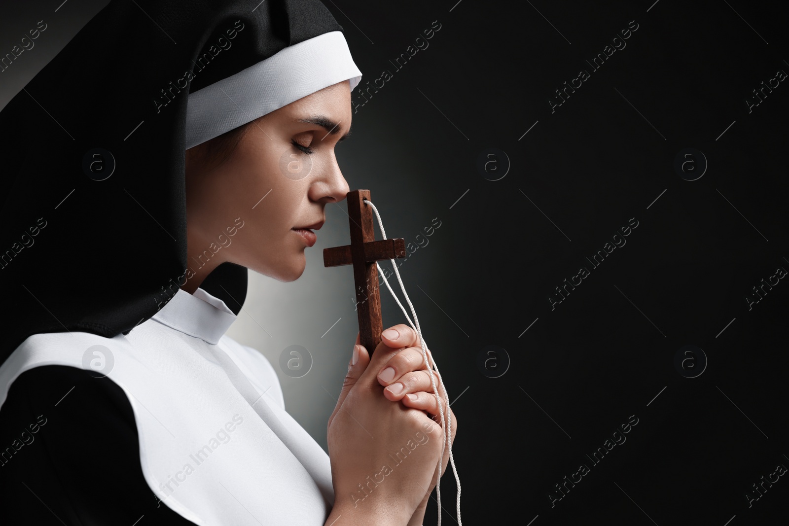 Photo of Nun with cross praying to God on black background. Space for text