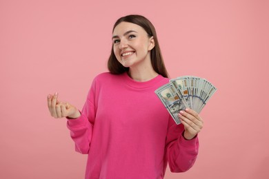 Photo of Happy woman with dollar banknotes showing money gesture on pink background